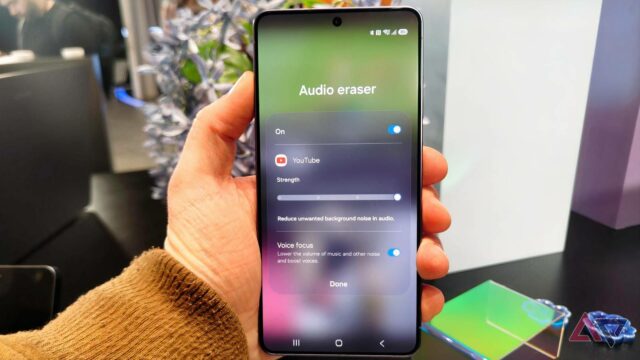 Um smartphone Galaxy S26 cercado por emojis raivosos e símbolos de fogo, sobrepostos com um carimbo vermelho 'CALM DOWN'