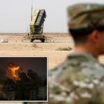 Um membro da Força Aérea dos EUA camuflado está em primeiro plano, de frente para uma bateria de mísseis Patriot na Base Aérea Prince Sultan, na Arábia Saudita.