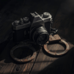 Escoteiro de modelos infantis de Michigan acusado de apostar milhões em casos de fraude. Uma câmera de filme vintage apoiada em uma superfície de madeira, posicionada entre um par de algemas de metal sob uma iluminação fraca e dramática.