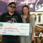 Jonathan G. e uma mulher segurando um cheque enorme de um milhão de dólares da Loteria do Colorado.
