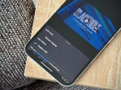 Experimentei o recurso mais recente do YouTube e foi tão surreal que pensei ter imaginado Mulher usando o telefone ao lado de um grande logotipo 3D do YouTube e de um ícone do aplicativo NotebookLM.