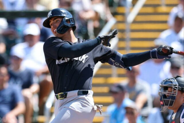Um rebatedor do New York Yankees com uma camisa azul marinho e um capacete preto, no meio do golpe durante o treinamento de primavera contra o Minnesota Twins.
