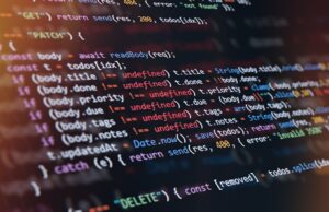 “Tokenmaxxing” está tornando os desenvolvedores menos produtivos do que pensam Close-up of computer screen showing colorful programming code lines with syntax highlighting and blurred light reflections.
