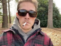 Influenciador ‘vivendo o sonho’ postando vídeos dele mesmo fumando e bebendo o dia todo Um homem de flanela fumando um cigarro lá fora.