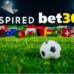 Inspired Entertainment estende parceria esportiva virtual com a bet365 antes da Copa do Mundo. Imagem mostrando os logotipos da Inspired Entertainment e da bet365 acima de um campo de futebol com uma bola de futebol em primeiro plano e uma fileira de bandeiras internacionais, representando uma parceria global de apostas esportivas virtuais.