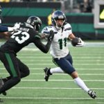 Dois jogadores de futebol, um com camisa branca e outro com camisa preta, em ação durante um jogo.