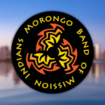 Juiz federal rejeita a tribo Morongo que contesta o processo das disposições do pacto de jogos da Califórnia. Morongo Band of Mission Indians logotipo circular com símbolo tribal vermelho e amarelo em fundo preto sobre o horizonte desfocado da cidade.