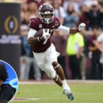 Um jogador de futebol masculino de camisa preta e shorts pega uma bola de futebol.