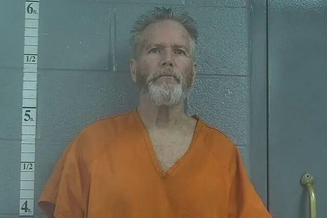 Mugshot de Richard Chesher, um homem com barba e cabelos grisalhos, vestindo um macacão laranja.