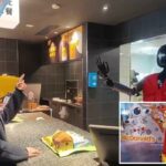 Uma mulher interagindo com um robô humanóide vestindo um colete do McDonald's em um balcão.