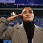 Um membro da segurança do hotel está ao lado de uma van da polícia na entrada do Royal Pines Resort, onde estão hospedados membros da seleção iraniana de futebol feminino, na Costa do Ouro, em 9 de março de 2026. A Austrália deve proteger a seleção iraniana de futebol feminino visitante, anunciou o filho do falecido xá do país em 9 de março, alertando sua recusa em cantar o hino nacional antes que uma partida pudesse ter