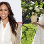 Meghan Markle em um vestido branco Brochu Walker, segurando um vaso de flores brancas.