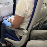 Passageiros sentados na cabine de um avião com cintos de segurança visíveis, espaço para as pernas e pertences pessoais durante um voo comercial