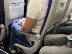 Meu voo será cancelado? O que saber sobre o conflito no Médio Oriente e os planos de voo Passageiros sentados na cabine de um avião com cintos de segurança visíveis, espaço para as pernas e pertences pessoais durante um voo comercial