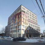 Edifício de vários andares com fachada de janelas retangulares em vários tons de marrom, vermelho e bege, com uma lateral do prédio com janelas todas retangulares.