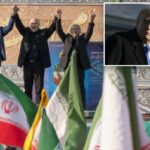 O presidente do Parlamento iraniano, Mohammad Bagher Ghalibaf, de mãos dadas com dois homens no palco de um comício pró-governo, com bandeiras iranianas em primeiro plano.