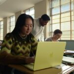 young woman seated at a classroom desk using a MacBook Neo
