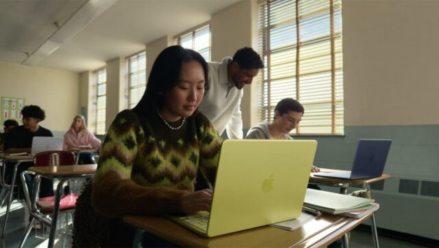 young woman seated at a classroom desk using a MacBook Neo