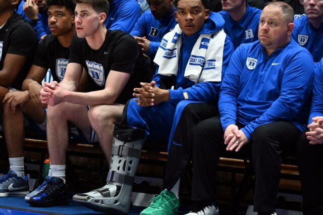 O guarda ferido do Duke Blue Devils, Caleb Foster, usando uma bota de caminhada no banco. O guarda ferido do Duke Blue Devils, Caleb Foster (centro), observa usando uma bota de caminhada durante o segundo tempo contra o North Carolina Tar Heels, no Cameron Indoor Stadium. 