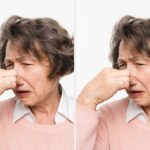 Três mulheres sorrindo em uma mesa de jantar, duas fazendo gestos brincalhões com as mãos. Copos e pratos são colocados na mesa em frente a eles