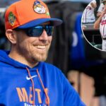 O técnico de rebatidas do New York Mets, Troy Snitker, sorrindo enquanto usava um boné de beisebol laranja e azul e um moletom azul.