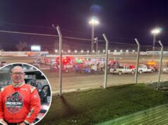 Oficial de corrida morre, outro ferido em acidente enquanto respondia a acidente em pista de terra Foto do oficial da corrida Billy Hurt em um traje de corrida vermelho ao lado de um veículo de corrida em pista de terra.