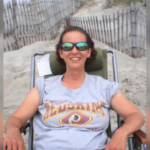 Operário da igreja de Luzerne condenado à prisão após roubar fundos para jogos de azar. Mulher usando óculos escuros relaxa em uma cadeira de praia em um caminho de duna arenosa, sorrindo enquanto veste uma camiseta cinza do Washington Redskins.