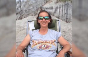 Operário da igreja de Luzerne condenado à prisão após roubar fundos para jogos de azar Operário da igreja de Luzerne condenado à prisão após roubar fundos para jogos de azar. Mulher usando óculos escuros relaxa em uma cadeira de praia em um caminho de duna arenosa, sorrindo enquanto veste uma camiseta cinza do Washington Redskins.