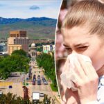 Jovem espirrando em um lenço de papel na frente de árvores floridas.