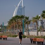 Um homem corre em uma praia com o hotel de luxo Burj Al Arab visto ao fundo em Dubai, Emirados Árabes Unidos, domingo, 1º de março de 2026.