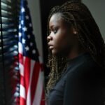 Retrato de uma jovem adolescente estressada olhando pela janela com uma bandeira americana ao fundo.