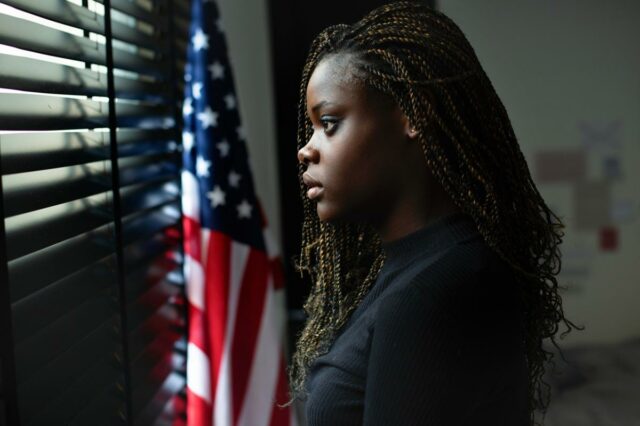 Retrato de uma jovem adolescente estressada olhando pela janela com uma bandeira americana ao fundo.