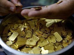 Ouro tem seu pior mês desde a recessão de 2008 – por que a guerra no Irã está atingindo os metais Uma mão coloca uma pequena barra de ouro em um recipiente cheio de várias barras e peças de ouro.