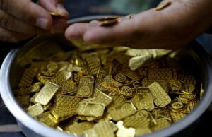 Ouro tem seu pior mês desde a recessão de 2008 – por que a guerra no Irã está atingindo os metais Uma mão coloca uma pequena barra de ouro em um recipiente cheio de várias barras e peças de ouro.