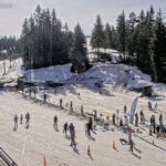 Uma movimentada estação de esqui com pessoas esquiando e praticando snowboard em um dia ensolarado.