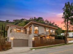 Por dentro do ambicioso projeto para construir casas verdadeiramente à prova de fogo após os devastadores incêndios em Palisades Uma casa de pedra com telhado de terracota, varandas e uma longa cerca de metal estampada na frente, com uma encosta de árvores verdes e arbustos atrás dela.