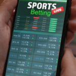 ACMA diz que as falhas das empresas de apostas minaram o sistema nacional de autoexclusão da BetStop. Mão segurando um smartphone exibindo uma interface de aplicativo de apostas esportivas com probabilidades ao vivo, listas de jogos e dados flutuantes de apostas.