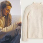 Uma modelo vestindo um suéter marfim com gola alta e uma minissaia de couro marrom, segurando uma pequena bolsa cilíndrica marrom de tartaruga.