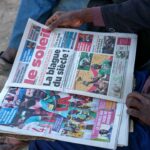 As pessoas lêem jornais que informam sobre a decisão da Confederação Africana de Futebol que retirou à selecção senegalesa o título da Taça das Nações Africanas e concedeu-o à selecção marroquina de futebol em Dakar, Senegal.