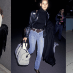 Uma convidada usa cabelo loiro na altura dos ombros em ondas soltas com uma parte central, óculos de sol retangulares estreitos com armação dourada fina e lentes marrons, um colar de ouro fino e uma pulseira de ouro, uma bolsa de couro preta com uma alça de corrente prateada grossa, um vestido sem mangas cinza com decote em V e cintura amarrada finalizado com uma bainha de lenço assimétrica em tecido leve drapeado, sapatos de bico fino com estampa de cobra, fora do Lafayette 148, durante a New York Fashion Week, em 11 de setembro, 2025 em Nova York, Nova York