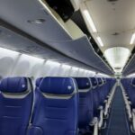 Interior de um avião vazio da Southwest Airlines com fileiras de assentos azuis e compartimentos superiores abertos.