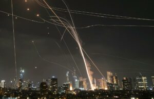 Terroristas do Hezbollah lançam 100 foguetes contra Israel – esmagando a Cúpula de Ferro Foto de longa exposição de mísseis e seus interceptadores no horizonte de uma cidade à noite.