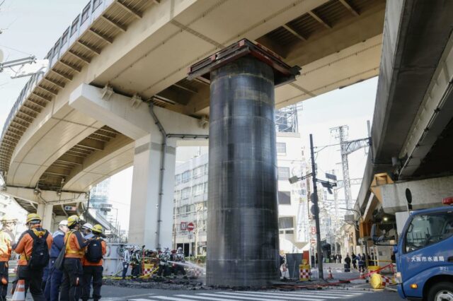 Pessoas com capacetes e coletes se reúnem em torno de um grande cano que emergiu do solo em um canteiro de obras de esgoto sob um viaduto em Osaka, no Japão.