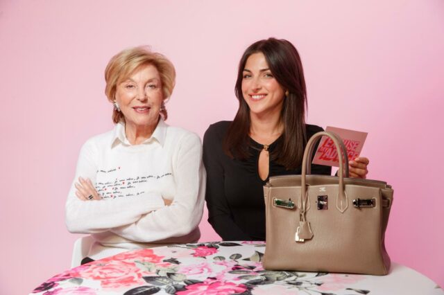 Uma jovem de jeans e camisa azul clara está sentada em um banquinho, segurando aberto um jornal do New York Post com a manchete 