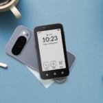 Mão segurando um Mudita Kompakt, apresentando um close de seu botão lateral físico e ícones de segurança flutuantes.