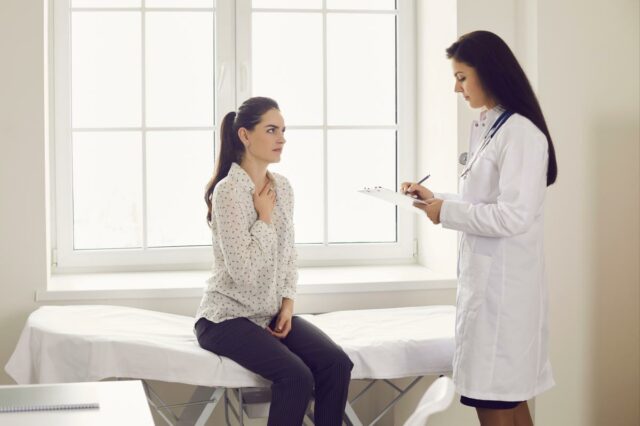 Uma jovem com uma longa trança e um suéter cinza tosse em sua mão.