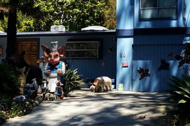 Uma casa azul com uma coleção de estátuas de porcos e decorações no jardim da frente.