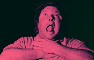 Você vai engasgar ao saber quantos empregos em tempo integral um data center de US$ 136 milhões realmente criará Um homem de cabelos cacheados é mostrado com a boca bem aberta e os olhos voltados para cima, segurando a garganta com as duas mãos, como se estivesse sufocando ou lutando para respirar. A imagem tem uma forte tonalidade vermelho-rosada e um fundo escuro.