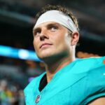 Close de um jogador do Miami Dolphins em uma camisa azul-petróleo e faixa branca, olhando para cima.