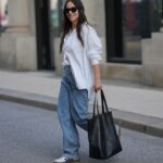 FRANKFURT AM MAIN, ALEMANHA - 26 DE MARÇO: Julia Kammerer é vista vestindo uma manga longa de algodão listrada horizontal rosa e bordô oversized da H&M; uma camisa de botão listrada azul e branca amarrada na cintura da JJXX; jeans de perna larga azul claro com corte descontraído da JJXX; tênis com cadarço de couro texturizado bordô e amarelo da Adidas; uma grande bolsa hobo de couro tecido cor de vinho da NA-KD; um boné de beisebol rosa claro com texto bordado em vermelho